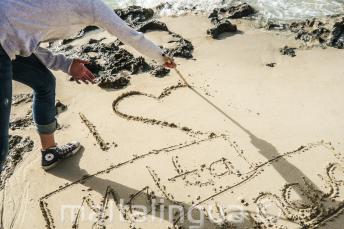 Un estudiante escribiendo "I LOVE" Maltalingua en la arena