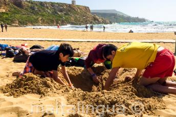 Jefe de grupo y estudiantes cavando un hoyo en la playa