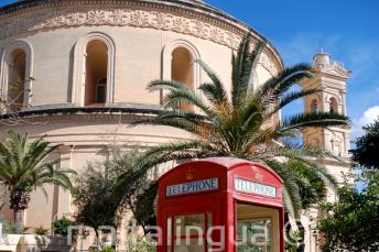 Una cabina de teléfono roja en frente de la rotonda de Mosta