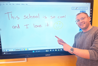 Un estudiante tras escribir una opinión positiva de la escuela en la pizarra