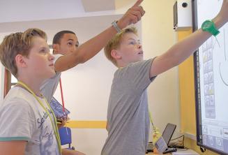 A teacher helping 2 students at an interactive whiteboard