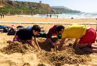 Jefe de grupo y estudiantes cavando un hoyo en la playa