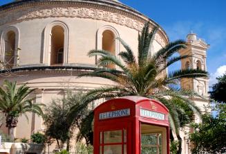 Una cabina de teléfono roja en frente de la rotonda de Mosta